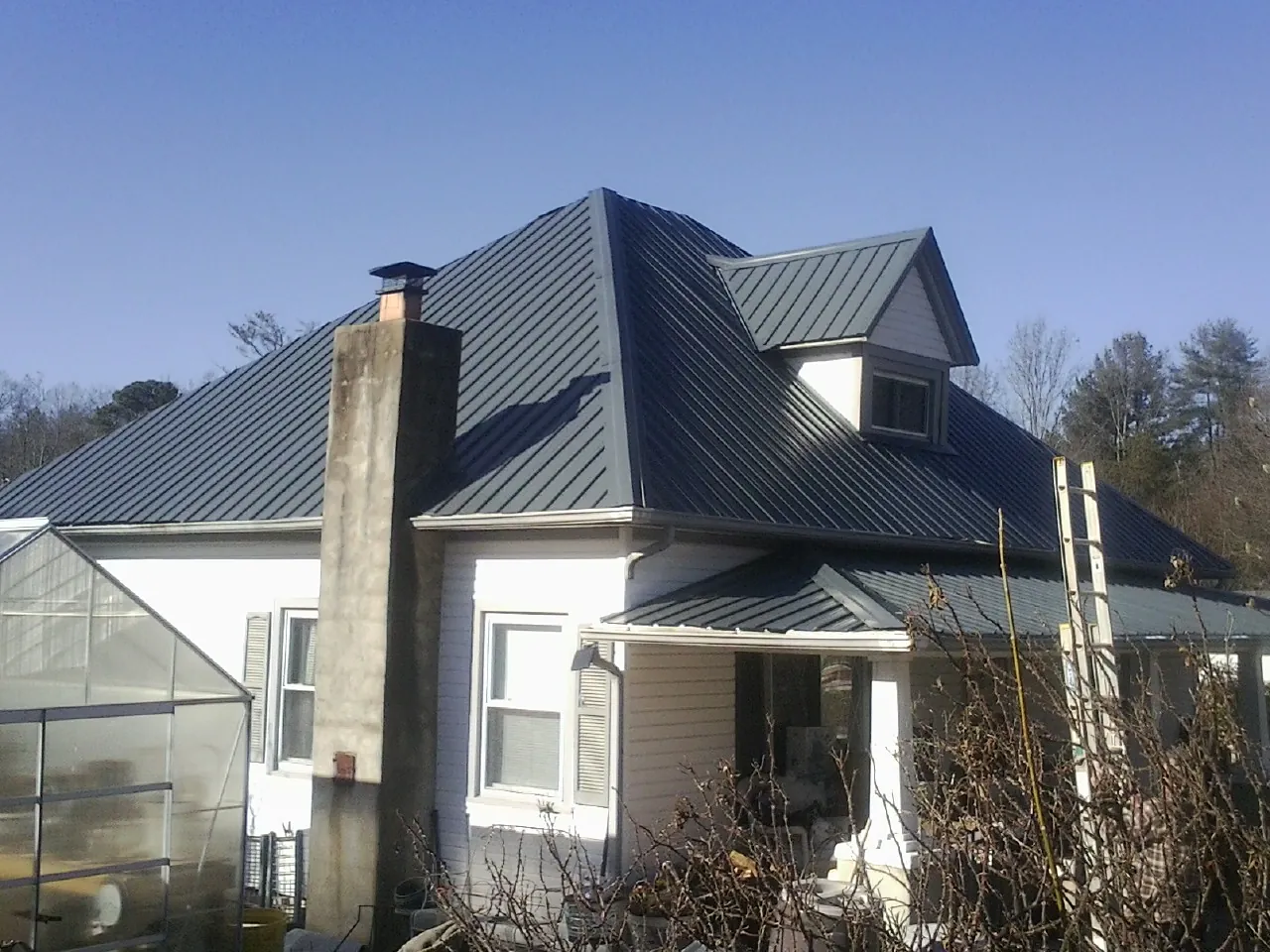 Dark blue standing seam metal roof on a white farmhouse with dormer — Slate & Tile Roof Repair by Roofing Brothers in Marina Del Rey